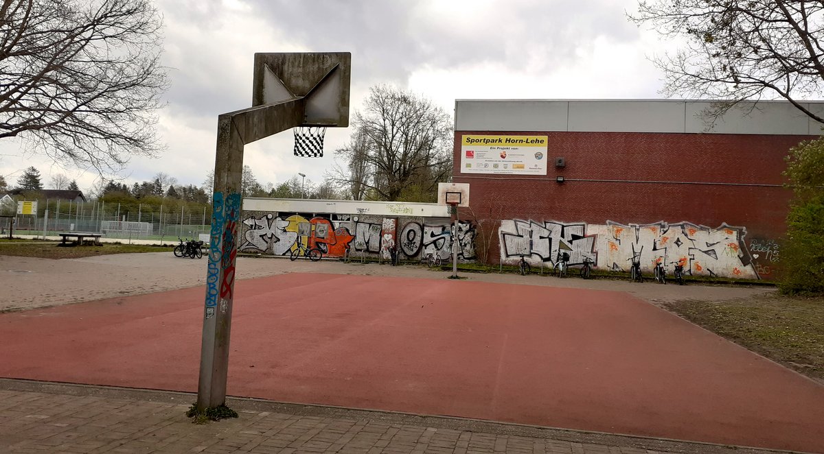 Foto von der Turnhalle in der Curiestraße, im Vordergrund ist ein Basketballplatz mit rotem Untergrund zu sehen.